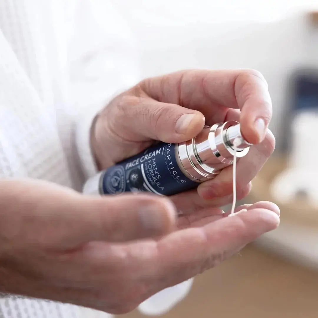 Person applying a face cream from a bottle labeled 'Men's Face Cream' on their hand.